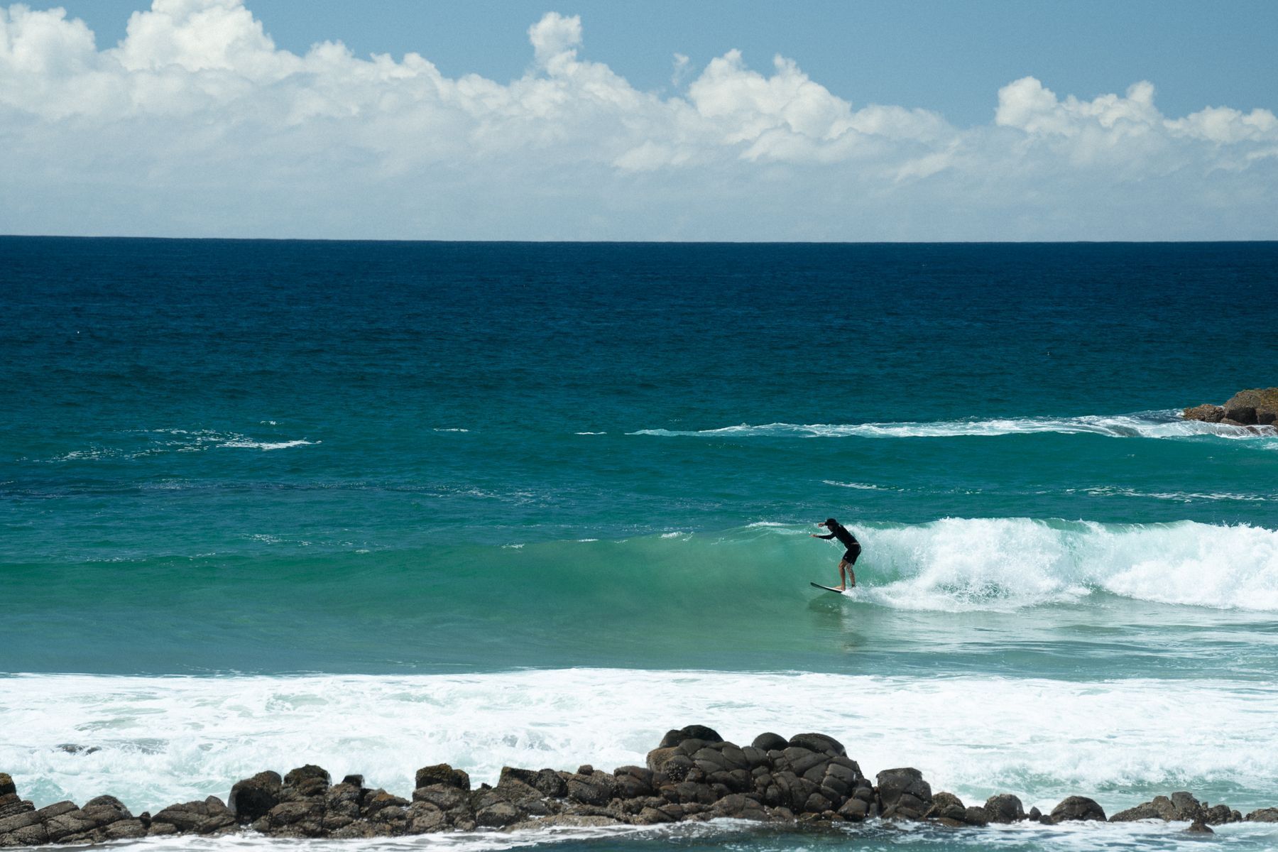 A surfer riding a wave off a sunny beach